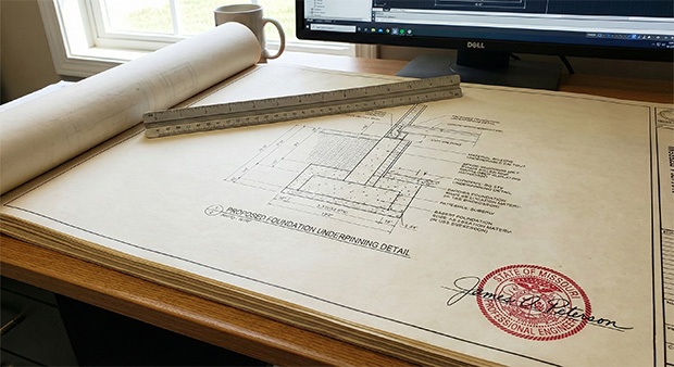 Blueprint of foundation details with engineering specifications, ruler, and computer in background, relevant to structural evaluations and reserve studies for homeowners associations.